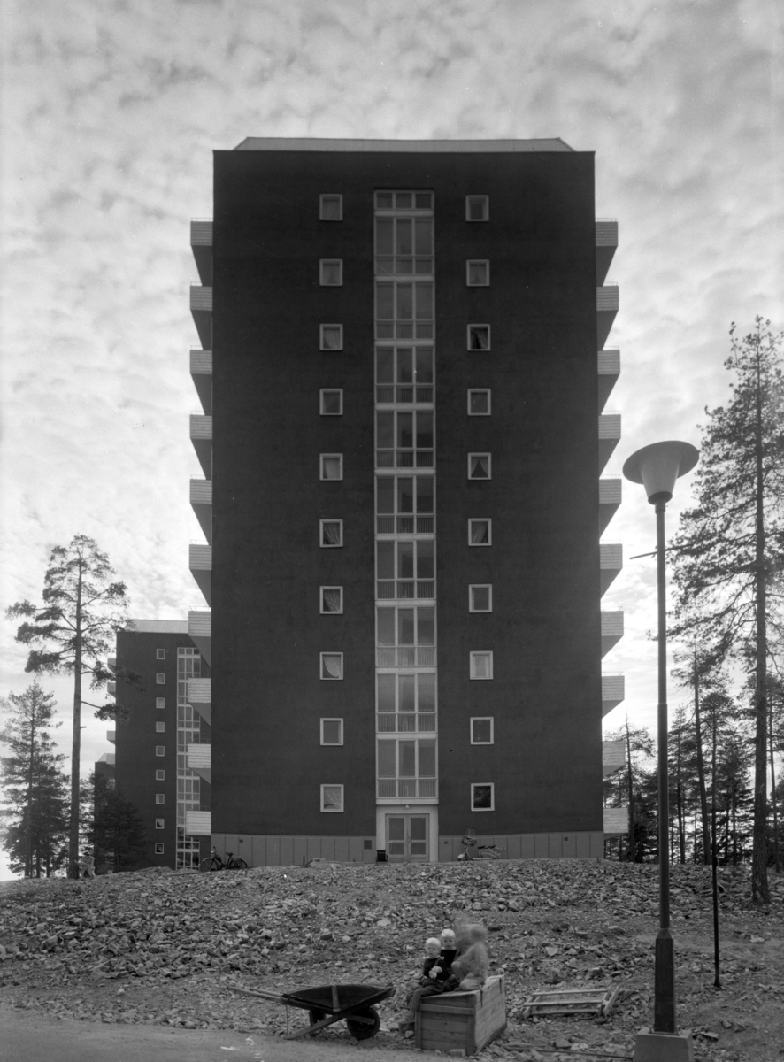 En av høyblokkene i drabantbybebyggelsen på Tonsenhagen i Grorudalen. Noen barn sitter utenfor blokka, de har med seg en trillebår av tre.