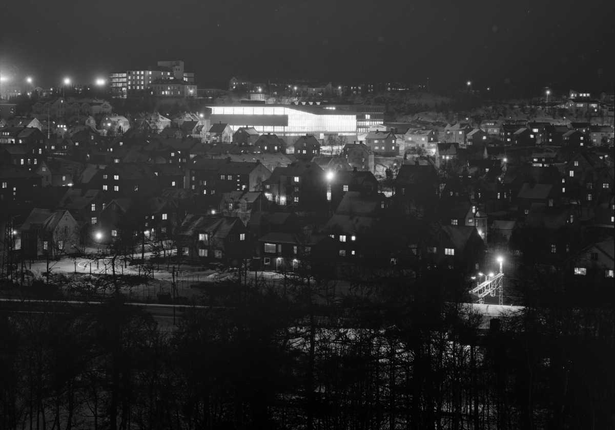 Foto av Idrettens hus i Narvik i mørket med bybebyggelse rundt.