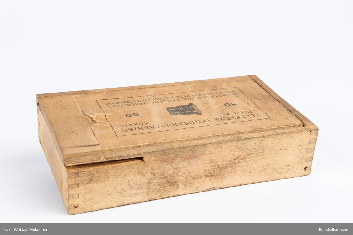 Treeske med skyvelokk, papirmerke med følgende påskrift (trykk): ELLEFSENS TENDSKRUEFABRIKK, STOKKE ST., NORWAY. 50 TENNSKRUER FOR BAKLADE-HVALKANON (DETONATORS FOR BREECH-LOADER WHALING GUN), samt bildet av en tennskrue.
Esken inneholder dessuten én stk tennskrue.