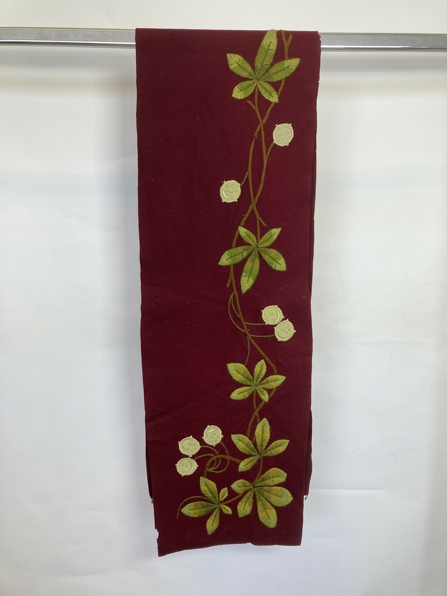 Ull, filt, ullgarn, silkegarn.
Løper ull, filt, dyprød.
Broderte bladranker, tre grønne
farger, en brun. Blomster hvit filt,
brodert med hvit silke, grønne ull
stilker.
Fire stykk messingringer på en kortside.