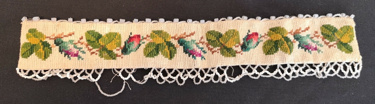 Brodert bånd i ullgarn og pyntet med perlekant.