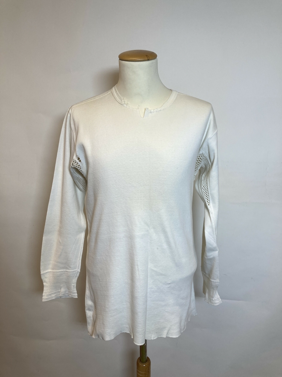 Trikot, glattstrikket.
Maskinstrikket og sydd.
Hvit, langarmet.
Åpent nettingmønster under armene.
Merket i nakken "KRONE"
Slitt, fillete.