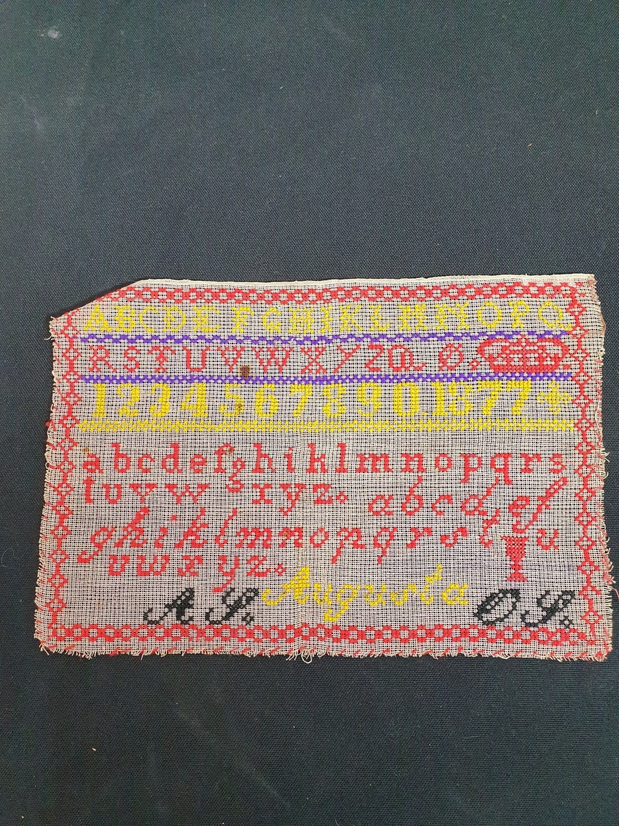 Beige strammei.
Brodert ulltråd, korssting.
Trå rød, gul, sort og lilla.
Brodert: to alfabeter, tall, krone, timeglass. 
"AS" "OS" "Augusta" "1877"