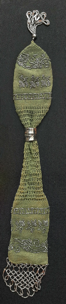 Heklet sylinder med åpning på langs på midtpartiet. Dekorert med metallperler og pyntet med perler på tråd i hver side.