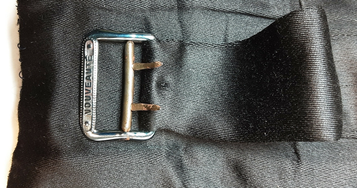 Vest med charleskrage. 3  stikklommer foran. Spensel i ryggen. Knappet foran med 4 knapper trukket med mønstret svart stoff. Hovedstoff framsiden av svart klede; ull, og rygg av silke. Helfóret med stripete bomullsstoff. Splitt bak