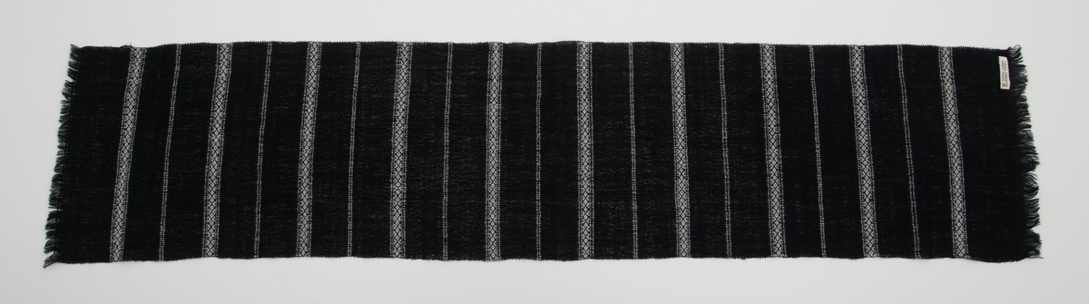 Svart vevd løper med innvevde striper i hvitt; regelmessig annenhver stripe med hvitt mønster og annenhver stripe med 2 hvite innslag.