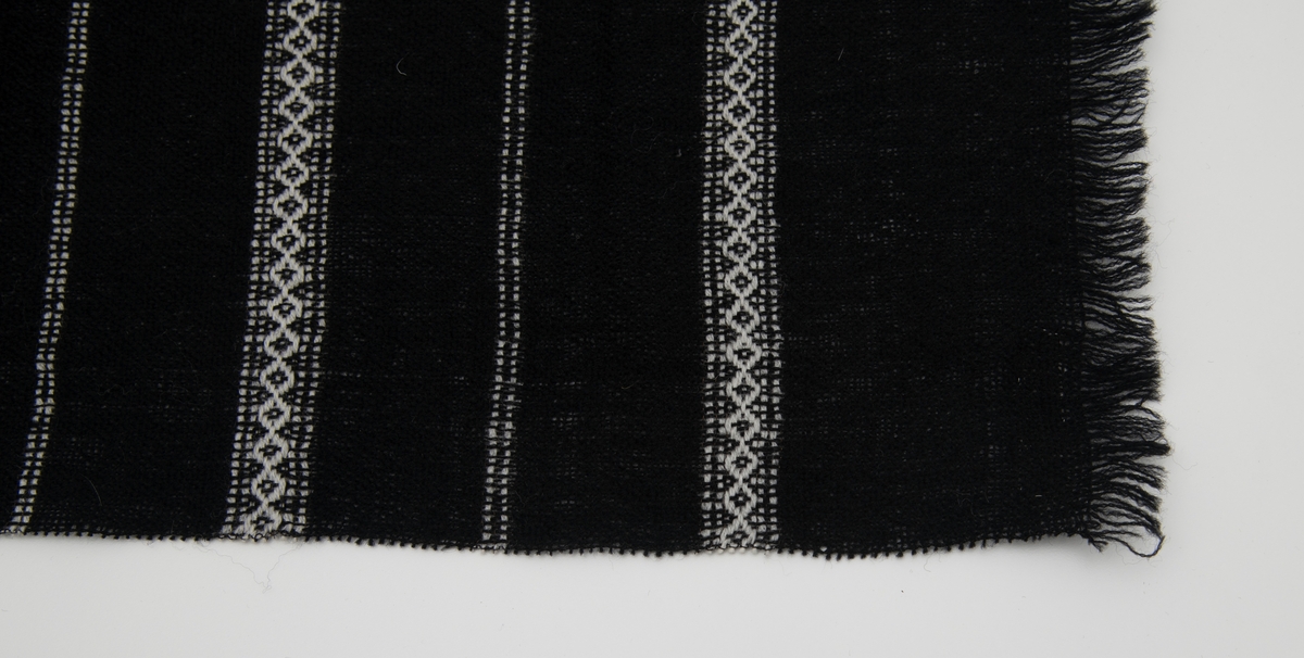Svart vevd løper med innvevde striper i hvitt; regelmessig annenhver stripe med hvitt mønster og annenhver stripe med 2 hvite innslag.
