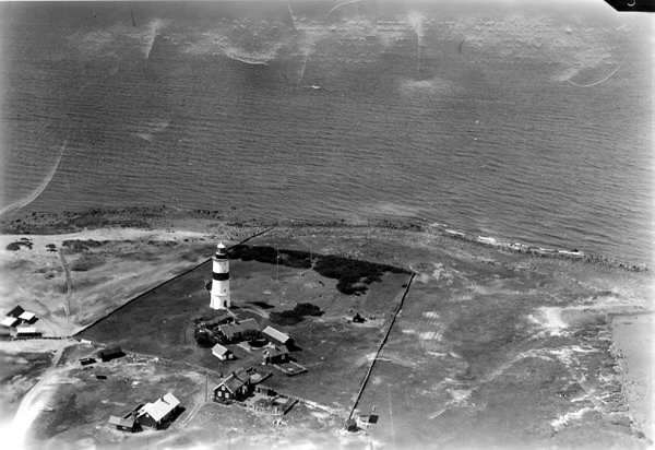 Flygbild över Morups Tånge fyr och bebyggelsen intill fyren med bostadshus, ekonomibyggnader och uthus. Stengärdesgårdar hägnar fyrområdet och man ser strandängarna ner mot havet.
Bild 1 är kolorerad och bilderna 2-3 är svartvita.