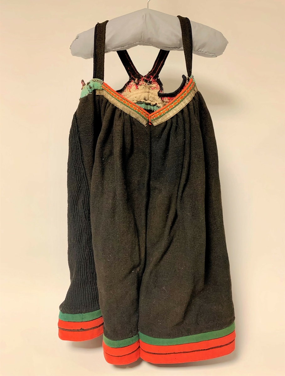 Svartstakk i vadmel med raudt liv i klede. På livet er det sauma på sylvbandt og ei svart list øvers med broderi. Svarte selar i vadmel. Det er ei grøn list mellom livet og stakken i grønt vadmel. På fronten av stakken oppe er det påsauma sylvband og ei grøn list med broderi. 
Stakken er plissert bak. Neders på stakken er det ei grøn og to raude listar i klede.
Stakken ber preg av slitasje.