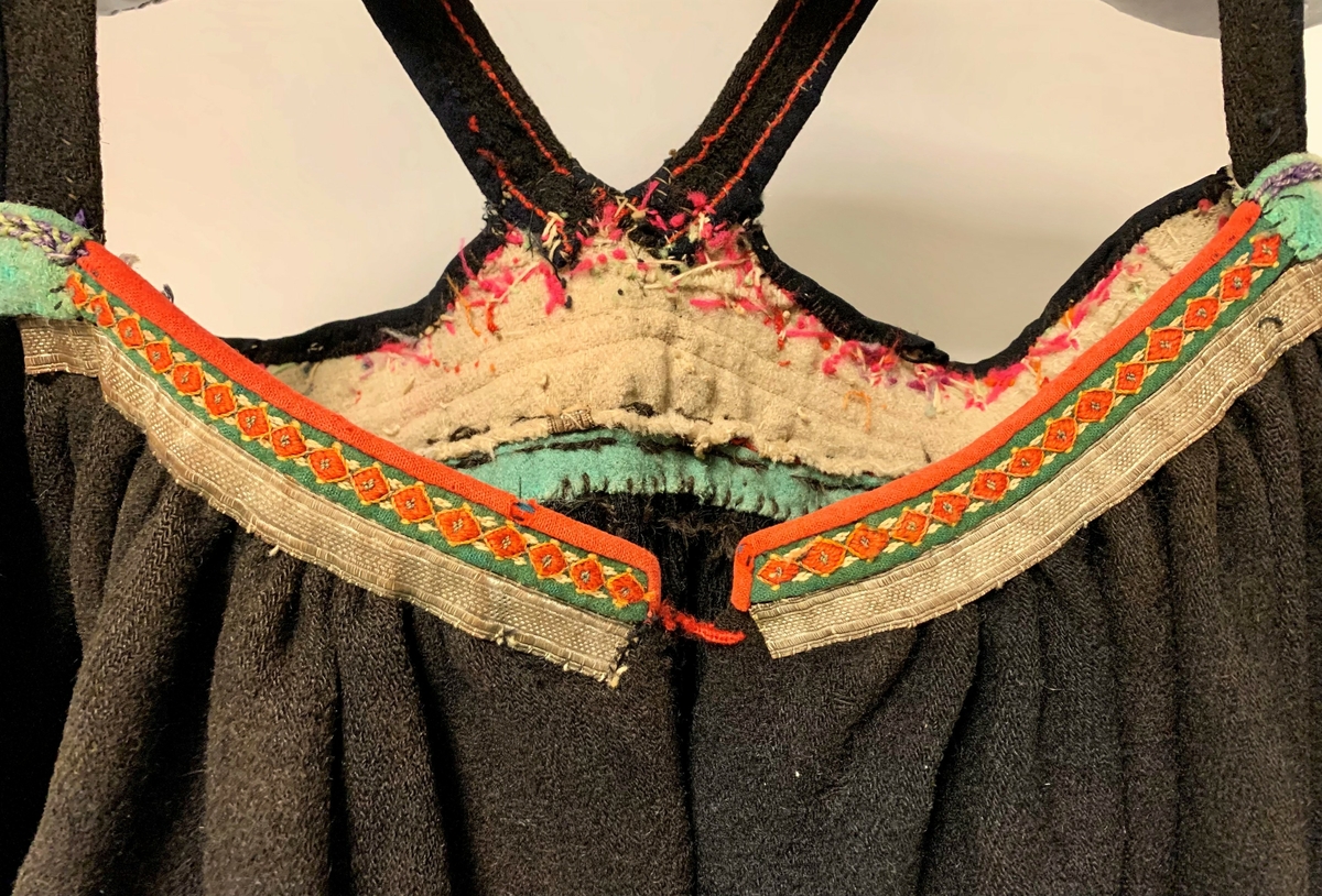 Svartstakk i vadmel med raudt liv i klede. På livet er det sauma på sylvbandt og ei svart list øvers med broderi. Svarte selar i vadmel. Det er ei grøn list mellom livet og stakken i grønt vadmel. På fronten av stakken oppe er det påsauma sylvband og ei grøn list med broderi. 
Stakken er plissert bak. Neders på stakken er det ei grøn og to raude listar i klede.
Stakken ber preg av slitasje.