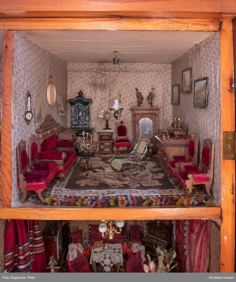 Inventering Sesam 1996-1999:
L 79 cm, B 46 cm, H 174 cm
Dockskåp av brunbetsat furu. Skåp med ett par glasdörrar med brun dekorrand på ramarna, undertill en låda med två dragknoppar, rakt krön med profilerad list. Skåpet står på fyra kulfötter. Dörrparet med lås och nyckel. På gavlarna 4 st fönster på vardera sidan. I skåpet 4 st våningar med sammanlagt 7 rum. Samtliga rum med mönstrade papperstapeter och krok i taket för lampa.
VÅNING 1: 1 rum, heltäckningsmatta av blåmönstrat tyg på vit botten. På höger kortvägg 3 st små pappersbilder i färgtryckav liten flicka i olika situationer. På  bakväggen en europakarta med tysk text.
VÅNING 2:  2 st rum. Bägge med mönstrade linoleummattor och två fönster. Gråmålad dörr mellan rummen. Vänster rum; Spiskåpa av vit papp på bakväggen. 2 st gardinlufter av vit spets med kornischer av gulmetall med påklistrad guldpappersremsa med mönster i relief. Höger rum; två gardinlufter av brunrandigt tyg, kornischer som ovan, omtag av metallkedjor på ena luften och rosa sidenband på andra. Ovanför dörren sitter 3 st beslag av pressad plåt. En större med måne och blommor och två mindre med sköld och blommor. 
VÅNING 3: bägge rummen med mönstrad heltäckningsmatta med lugg och två fönster. Vänster rum; 2 gardinlufter, 1 sänghimmel och 1 draperi av blått siden med vit kantspets. Gardiner med kornischer som ovan. 5 st omtag i form av snodd av gulmetall. Höger rum; enfärgade röda tapeter,2 st gardinlufter av rödrandigt siden med omtag av samma tyg, undergardin av vit spets, kornischer som ovan. Ett draperi av rött och randigt (i flera färger) ylle med ett omtag av metallkedja.
VÅNING 4: Vänster rum; flerfärgat och småmönstrad linoleummatta, Höger rum; utan golvbeläggning. 
- Ett par gröna gardiner av stärkt bomull, som ursprunglingen har suttit innanför glasdörrarna på dockskåpet. Rynkade i båda kortändorna. B 46,5, L 128 cm
Har tillhört givaren. (född 1886 enl. adelskalendern). 
Inventarier till dockskåpet inv.nr 164571-164728
Leif Wallin nov 1997