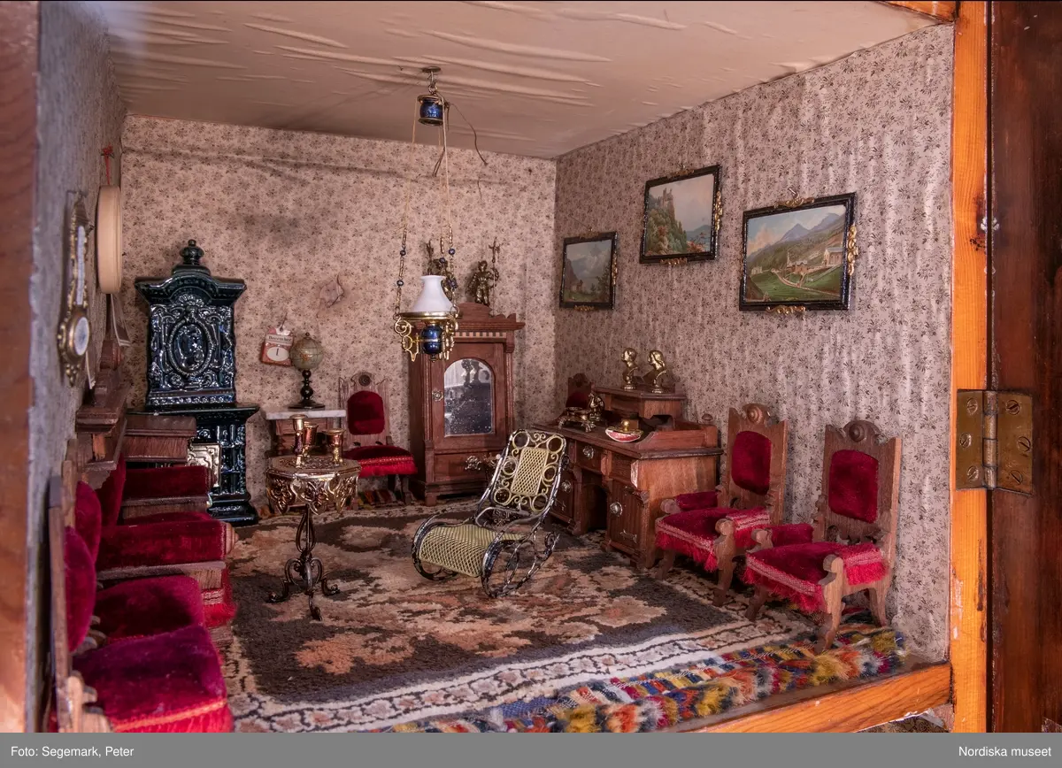 Inventering Sesam 1996-1999:
L 79 cm, B 46 cm, H 174 cm
Dockskåp av brunbetsat furu. Skåp med ett par glasdörrar med brun dekorrand på ramarna, undertill en låda med två dragknoppar, rakt krön med profilerad list. Skåpet står på fyra kulfötter. Dörrparet med lås och nyckel. På gavlarna 4 st fönster på vardera sidan. I skåpet 4 st våningar med sammanlagt 7 rum. Samtliga rum med mönstrade papperstapeter och krok i taket för lampa.
VÅNING 1: 1 rum, heltäckningsmatta av blåmönstrat tyg på vit botten. På höger kortvägg 3 st små pappersbilder i färgtryckav liten flicka i olika situationer. På  bakväggen en europakarta med tysk text.
VÅNING 2:  2 st rum. Bägge med mönstrade linoleummattor och två fönster. Gråmålad dörr mellan rummen. Vänster rum; Spiskåpa av vit papp på bakväggen. 2 st gardinlufter av vit spets med kornischer av gulmetall med påklistrad guldpappersremsa med mönster i relief. Höger rum; två gardinlufter av brunrandigt tyg, kornischer som ovan, omtag av metallkedjor på ena luften och rosa sidenband på andra. Ovanför dörren sitter 3 st beslag av pressad plåt. En större med måne och blommor och två mindre med sköld och blommor. 
VÅNING 3: bägge rummen med mönstrad heltäckningsmatta med lugg och två fönster. Vänster rum; 2 gardinlufter, 1 sänghimmel och 1 draperi av blått siden med vit kantspets. Gardiner med kornischer som ovan. 5 st omtag i form av snodd av gulmetall. Höger rum; enfärgade röda tapeter,2 st gardinlufter av rödrandigt siden med omtag av samma tyg, undergardin av vit spets, kornischer som ovan. Ett draperi av rött och randigt (i flera färger) ylle med ett omtag av metallkedja.
VÅNING 4: Vänster rum; flerfärgat och småmönstrad linoleummatta, Höger rum; utan golvbeläggning. 
- Ett par gröna gardiner av stärkt bomull, som ursprunglingen har suttit innanför glasdörrarna på dockskåpet. Rynkade i båda kortändorna. B 46,5, L 128 cm
Har tillhört givaren. (född 1886 enl. adelskalendern). 
Inventarier till dockskåpet inv.nr 164571-164728
Leif Wallin nov 1997