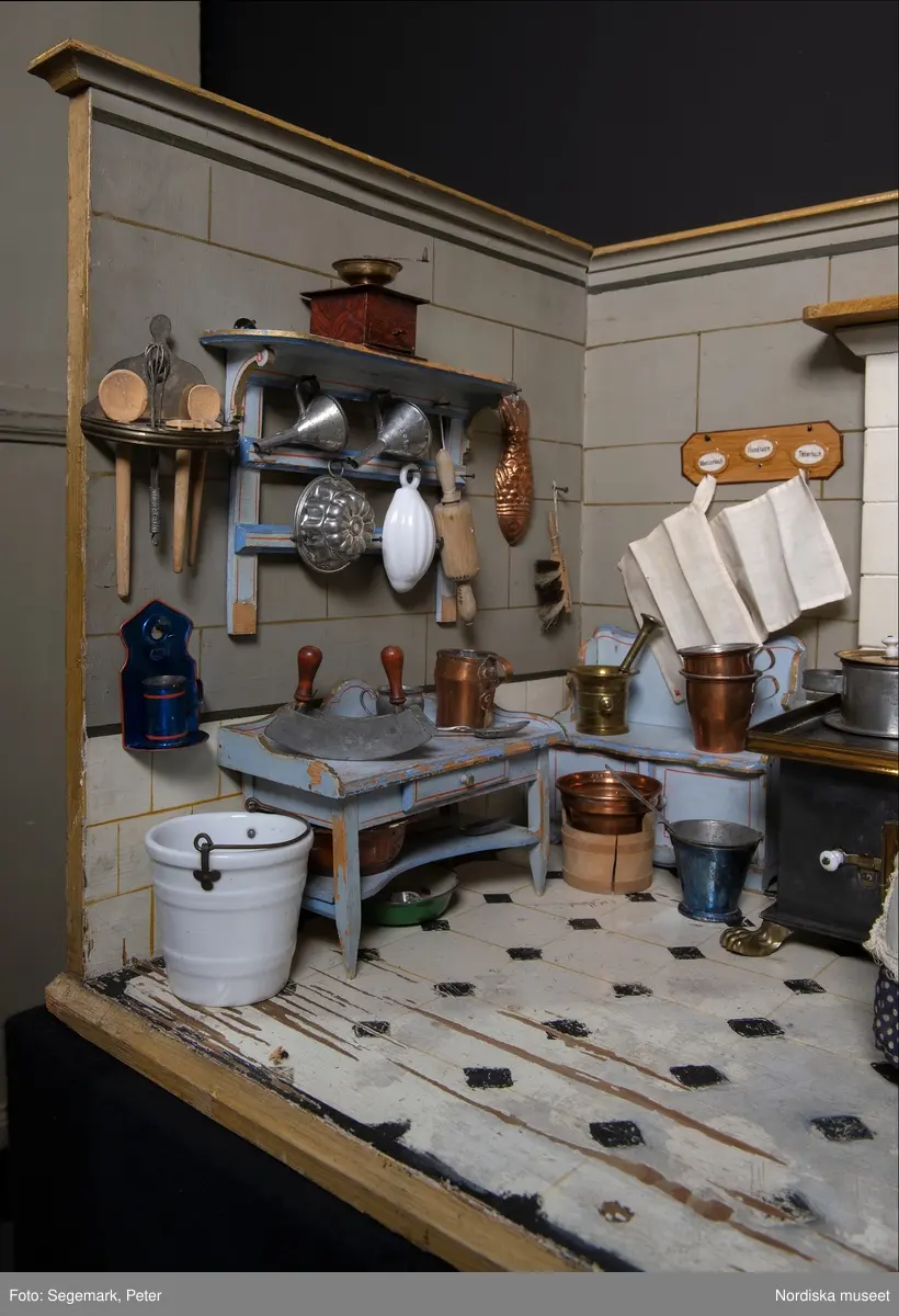 Inventering Sesam 1996-1999:
L 88  H 43,5  Dj 44   cm
Dockskåp, köksdockskåp, av trä, skafferi och kök, utvändigt träådrat. Väggarna i köket kvadermålade och golvet svart och vitrutigt. Skafferiets väggar rosa, väggfasta hyllor, dörrposten ekimiterad.
Lös inredning se inv. 192.992-193.058
Birgitta Martinius 1996