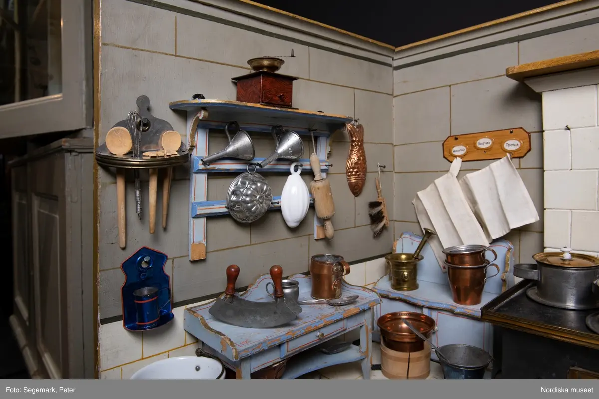 Inventering Sesam 1996-1999:
L 88  H 43,5  Dj 44   cm
Dockskåp, köksdockskåp, av trä, skafferi och kök, utvändigt träådrat. Väggarna i köket kvadermålade och golvet svart och vitrutigt. Skafferiets väggar rosa, väggfasta hyllor, dörrposten ekimiterad.
Lös inredning se inv. 192.992-193.058
Birgitta Martinius 1996