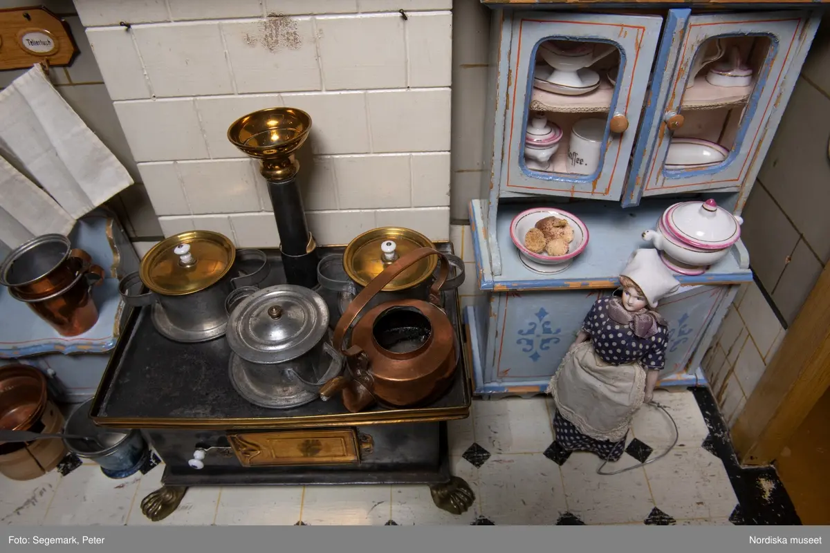 Inventering Sesam 1996-1999:
L 88  H 43,5  Dj 44   cm
Dockskåp, köksdockskåp, av trä, skafferi och kök, utvändigt träådrat. Väggarna i köket kvadermålade och golvet svart och vitrutigt. Skafferiets väggar rosa, väggfasta hyllor, dörrposten ekimiterad.
Lös inredning se inv. 192.992-193.058
Birgitta Martinius 1996