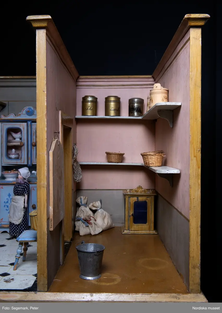 Inventering Sesam 1996-1999:
L 88  H 43,5  Dj 44   cm
Dockskåp, köksdockskåp, av trä, skafferi och kök, utvändigt träådrat. Väggarna i köket kvadermålade och golvet svart och vitrutigt. Skafferiets väggar rosa, väggfasta hyllor, dörrposten ekimiterad.
Lös inredning se inv. 192.992-193.058
Birgitta Martinius 1996