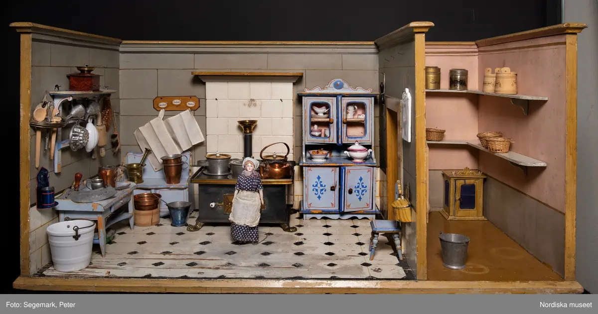 Inventering Sesam 1996-1999:
L 88  H 43,5  Dj 44   cm
Dockskåp, köksdockskåp, av trä, skafferi och kök, utvändigt träådrat. Väggarna i köket kvadermålade och golvet svart och vitrutigt. Skafferiets väggar rosa, väggfasta hyllor, dörrposten ekimiterad.
Lös inredning se inv. 192.992-193.058
Birgitta Martinius 1996