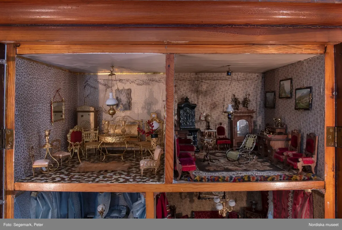 Inventering Sesam 1996-1999:
L 79 cm, B 46 cm, H 174 cm
Dockskåp av brunbetsat furu. Skåp med ett par glasdörrar med brun dekorrand på ramarna, undertill en låda med två dragknoppar, rakt krön med profilerad list. Skåpet står på fyra kulfötter. Dörrparet med lås och nyckel. På gavlarna 4 st fönster på vardera sidan. I skåpet 4 st våningar med sammanlagt 7 rum. Samtliga rum med mönstrade papperstapeter och krok i taket för lampa.
VÅNING 1: 1 rum, heltäckningsmatta av blåmönstrat tyg på vit botten. På höger kortvägg 3 st små pappersbilder i färgtryckav liten flicka i olika situationer. På  bakväggen en europakarta med tysk text.
VÅNING 2:  2 st rum. Bägge med mönstrade linoleummattor och två fönster. Gråmålad dörr mellan rummen. Vänster rum; Spiskåpa av vit papp på bakväggen. 2 st gardinlufter av vit spets med kornischer av gulmetall med påklistrad guldpappersremsa med mönster i relief. Höger rum; två gardinlufter av brunrandigt tyg, kornischer som ovan, omtag av metallkedjor på ena luften och rosa sidenband på andra. Ovanför dörren sitter 3 st beslag av pressad plåt. En större med måne och blommor och två mindre med sköld och blommor. 
VÅNING 3: bägge rummen med mönstrad heltäckningsmatta med lugg och två fönster. Vänster rum; 2 gardinlufter, 1 sänghimmel och 1 draperi av blått siden med vit kantspets. Gardiner med kornischer som ovan. 5 st omtag i form av snodd av gulmetall. Höger rum; enfärgade röda tapeter,2 st gardinlufter av rödrandigt siden med omtag av samma tyg, undergardin av vit spets, kornischer som ovan. Ett draperi av rött och randigt (i flera färger) ylle med ett omtag av metallkedja.
VÅNING 4: Vänster rum; flerfärgat och småmönstrad linoleummatta, Höger rum; utan golvbeläggning. 
- Ett par gröna gardiner av stärkt bomull, som ursprunglingen har suttit innanför glasdörrarna på dockskåpet. Rynkade i båda kortändorna. B 46,5, L 128 cm
Har tillhört givaren. (född 1886 enl. adelskalendern). 
Inventarier till dockskåpet inv.nr 164571-164728
Leif Wallin nov 1997