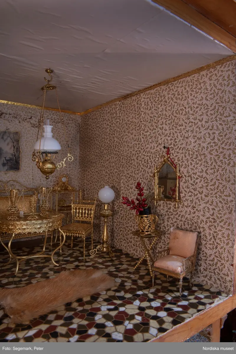 Inventering Sesam 1996-1999:
L 79 cm, B 46 cm, H 174 cm
Dockskåp av brunbetsat furu. Skåp med ett par glasdörrar med brun dekorrand på ramarna, undertill en låda med två dragknoppar, rakt krön med profilerad list. Skåpet står på fyra kulfötter. Dörrparet med lås och nyckel. På gavlarna 4 st fönster på vardera sidan. I skåpet 4 st våningar med sammanlagt 7 rum. Samtliga rum med mönstrade papperstapeter och krok i taket för lampa.
VÅNING 1: 1 rum, heltäckningsmatta av blåmönstrat tyg på vit botten. På höger kortvägg 3 st små pappersbilder i färgtryckav liten flicka i olika situationer. På  bakväggen en europakarta med tysk text.
VÅNING 2:  2 st rum. Bägge med mönstrade linoleummattor och två fönster. Gråmålad dörr mellan rummen. Vänster rum; Spiskåpa av vit papp på bakväggen. 2 st gardinlufter av vit spets med kornischer av gulmetall med påklistrad guldpappersremsa med mönster i relief. Höger rum; två gardinlufter av brunrandigt tyg, kornischer som ovan, omtag av metallkedjor på ena luften och rosa sidenband på andra. Ovanför dörren sitter 3 st beslag av pressad plåt. En större med måne och blommor och två mindre med sköld och blommor. 
VÅNING 3: bägge rummen med mönstrad heltäckningsmatta med lugg och två fönster. Vänster rum; 2 gardinlufter, 1 sänghimmel och 1 draperi av blått siden med vit kantspets. Gardiner med kornischer som ovan. 5 st omtag i form av snodd av gulmetall. Höger rum; enfärgade röda tapeter,2 st gardinlufter av rödrandigt siden med omtag av samma tyg, undergardin av vit spets, kornischer som ovan. Ett draperi av rött och randigt (i flera färger) ylle med ett omtag av metallkedja.
VÅNING 4: Vänster rum; flerfärgat och småmönstrad linoleummatta, Höger rum; utan golvbeläggning. 
- Ett par gröna gardiner av stärkt bomull, som ursprunglingen har suttit innanför glasdörrarna på dockskåpet. Rynkade i båda kortändorna. B 46,5, L 128 cm
Har tillhört givaren. (född 1886 enl. adelskalendern). 
Inventarier till dockskåpet inv.nr 164571-164728
Leif Wallin nov 1997