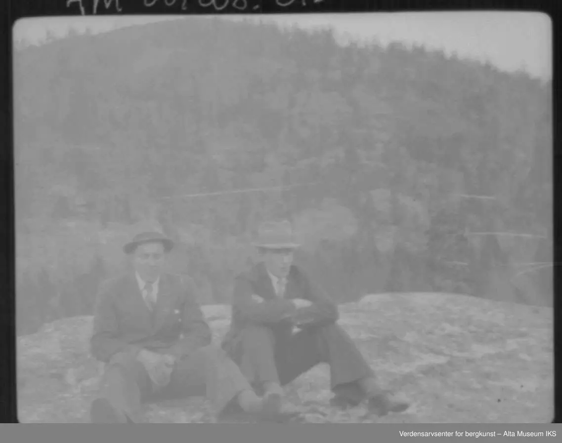 2 menn med dress og hatt sitter på et fjell.