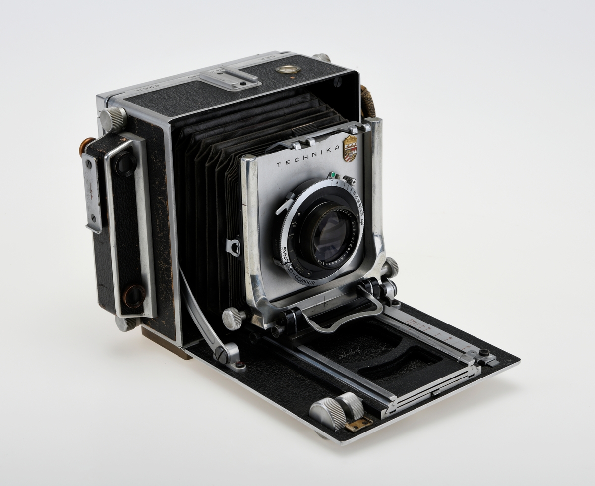 Et storformat belgkamera for plater på 9x12cm fra Linhof, med et 150mm fastobjektiv. Linhof er i dag den eldste kameraprodusenten i verden som fortsatt produserer kameraer etter at Gandolfi og Kodak sluttet deres produksjon.    

Foran på kameraet er det en luke som kan åpnes opp for å dra fram belgen som er festet på en skinne på innsiden av luken. Belgen kan flyttes fram og tilbake på skinnen, og objektivplaten kan også flyttes sideveis, i høyden eller tippes bakover. Objektivet og lukkerhuset er montert på en avtagbar plate i front av belgen. På lukkerhuset er det et hjul for å stille inn lukkertiden og en liten spake for å justere blenderåpningen. 

På baksiden av kameraet er det en luke til filmplater med en mattskive inni. På luken er det en svart solskjerm som kan brettes ut. På den en siden av kamerahuset er det en søker med en rammesøkermekanisme koblet til fokusmekanismen foran på belgskinnen. Søkeren har en holder til en blitslampe. På toppen av kamerahuset er det en tilbehørssko og et vater. Kameraet er dekket i svart skinn. Håndtak i skinn på siden. kameraet har stativfester både under kamerahuset og under luken til belgen.