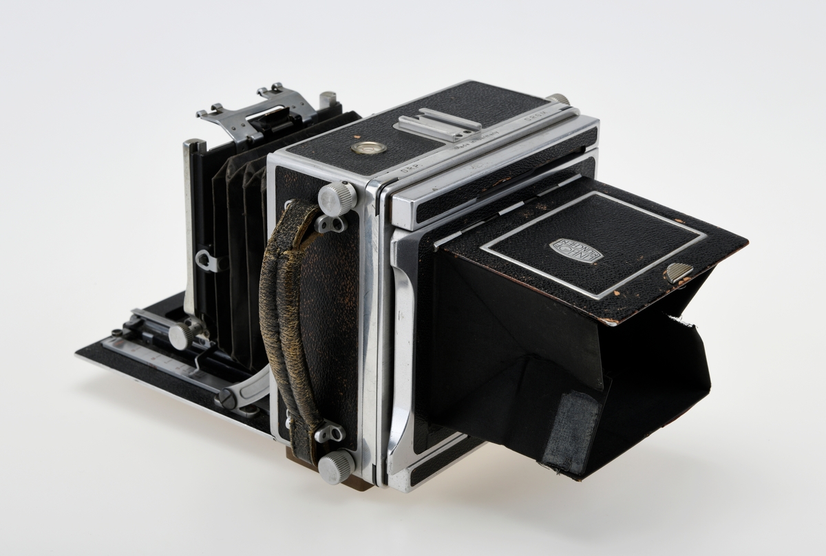 Et storformat belgkamera for plater på 9x12cm fra Linhof, med et 150mm fastobjektiv. Linhof er i dag den eldste kameraprodusenten i verden som fortsatt produserer kameraer etter at Gandolfi og Kodak sluttet deres produksjon.    

Foran på kameraet er det en luke som kan åpnes opp for å dra fram belgen som er festet på en skinne på innsiden av luken. Belgen kan flyttes fram og tilbake på skinnen, og objektivplaten kan også flyttes sideveis, i høyden eller tippes bakover. Objektivet og lukkerhuset er montert på en avtagbar plate i front av belgen. På lukkerhuset er det et hjul for å stille inn lukkertiden og en liten spake for å justere blenderåpningen. 

På baksiden av kameraet er det en luke til filmplater med en mattskive inni. På luken er det en svart solskjerm som kan brettes ut. På den en siden av kamerahuset er det en søker med en rammesøkermekanisme koblet til fokusmekanismen foran på belgskinnen. Søkeren har en holder til en blitslampe. På toppen av kamerahuset er det en tilbehørssko og et vater. Kameraet er dekket i svart skinn. Håndtak i skinn på siden. kameraet har stativfester både under kamerahuset og under luken til belgen.
