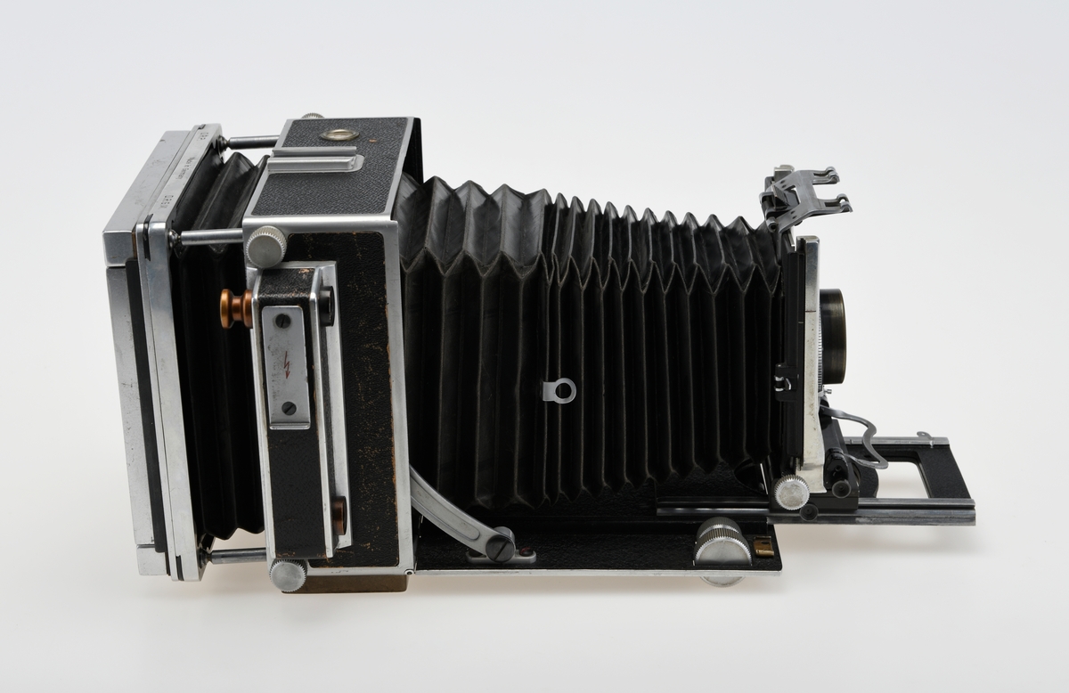 Et storformat belgkamera for plater på 9x12cm fra Linhof, med et 150mm fastobjektiv. Linhof er i dag den eldste kameraprodusenten i verden som fortsatt produserer kameraer etter at Gandolfi og Kodak sluttet deres produksjon.    

Foran på kameraet er det en luke som kan åpnes opp for å dra fram belgen som er festet på en skinne på innsiden av luken. Belgen kan flyttes fram og tilbake på skinnen, og objektivplaten kan også flyttes sideveis, i høyden eller tippes bakover. Objektivet og lukkerhuset er montert på en avtagbar plate i front av belgen. På lukkerhuset er det et hjul for å stille inn lukkertiden og en liten spake for å justere blenderåpningen. 

På baksiden av kameraet er det en luke til filmplater med en mattskive inni. På luken er det en svart solskjerm som kan brettes ut. På den en siden av kamerahuset er det en søker med en rammesøkermekanisme koblet til fokusmekanismen foran på belgskinnen. Søkeren har en holder til en blitslampe. På toppen av kamerahuset er det en tilbehørssko og et vater. Kameraet er dekket i svart skinn. Håndtak i skinn på siden. kameraet har stativfester både under kamerahuset og under luken til belgen.