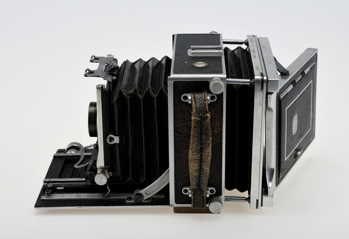 Et storformat belgkamera for plater på 9x12cm fra Linhof, med et 150mm fastobjektiv. Linhof er i dag den eldste kameraprodusenten i verden som fortsatt produserer kameraer etter at Gandolfi og Kodak sluttet deres produksjon.    

Foran på kameraet er det en luke som kan åpnes opp for å dra fram belgen som er festet på en skinne på innsiden av luken. Belgen kan flyttes fram og tilbake på skinnen, og objektivplaten kan også flyttes sideveis, i høyden eller tippes bakover. Objektivet og lukkerhuset er montert på en avtagbar plate i front av belgen. På lukkerhuset er det et hjul for å stille inn lukkertiden og en liten spake for å justere blenderåpningen. 

På baksiden av kameraet er det en luke til filmplater med en mattskive inni. På luken er det en svart solskjerm som kan brettes ut. På den en siden av kamerahuset er det en søker med en rammesøkermekanisme koblet til fokusmekanismen foran på belgskinnen. Søkeren har en holder til en blitslampe. På toppen av kamerahuset er det en tilbehørssko og et vater. Kameraet er dekket i svart skinn. Håndtak i skinn på siden. kameraet har stativfester både under kamerahuset og under luken til belgen.
