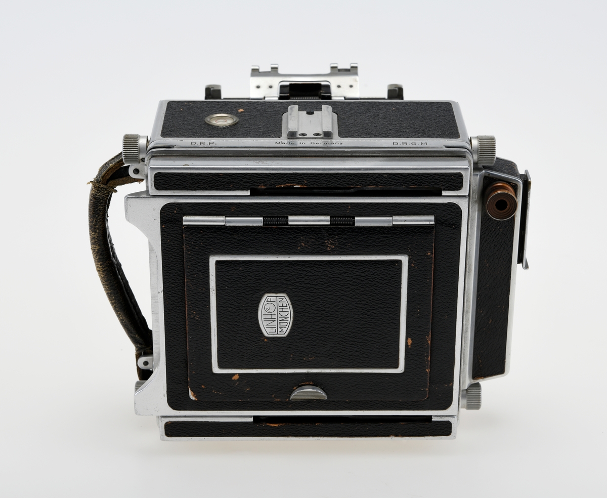 Et storformat belgkamera for plater på 9x12cm fra Linhof, med et 150mm fastobjektiv. Linhof er i dag den eldste kameraprodusenten i verden som fortsatt produserer kameraer etter at Gandolfi og Kodak sluttet deres produksjon.    

Foran på kameraet er det en luke som kan åpnes opp for å dra fram belgen som er festet på en skinne på innsiden av luken. Belgen kan flyttes fram og tilbake på skinnen, og objektivplaten kan også flyttes sideveis, i høyden eller tippes bakover. Objektivet og lukkerhuset er montert på en avtagbar plate i front av belgen. På lukkerhuset er det et hjul for å stille inn lukkertiden og en liten spake for å justere blenderåpningen. 

På baksiden av kameraet er det en luke til filmplater med en mattskive inni. På luken er det en svart solskjerm som kan brettes ut. På den en siden av kamerahuset er det en søker med en rammesøkermekanisme koblet til fokusmekanismen foran på belgskinnen. Søkeren har en holder til en blitslampe. På toppen av kamerahuset er det en tilbehørssko og et vater. Kameraet er dekket i svart skinn. Håndtak i skinn på siden. kameraet har stativfester både under kamerahuset og under luken til belgen.