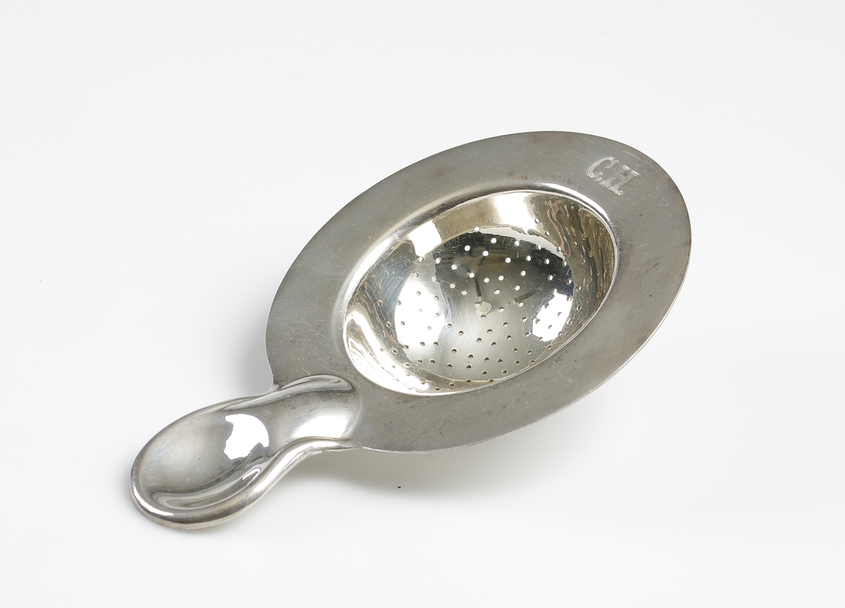 En rund tesil av nysilver med runt slätt handtag, märkt: "C.H." på brämen. Stämpel på skaftets undersida "ART.KRUPP. BERNDORF".