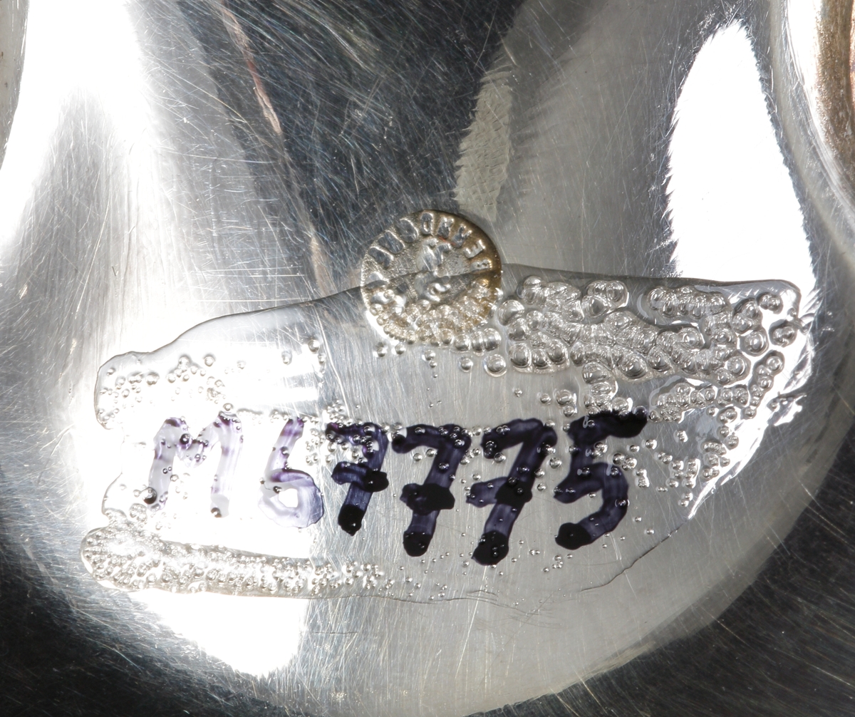 En rund tesil av nysilver med runt slätt handtag, märkt: "C.H." på brämen. Stämpel på skaftets undersida "ART.KRUPP. BERNDORF".