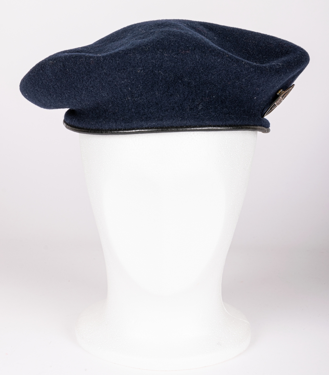 Blå filtbasker med läderkant. I sidan en metallpin "Var redo". Invändigt tryck: The Scout Shop, Trade Mark "Boy scouts" KANGOL, Cleaton Cumberland".
Storlek 7½/58.
Tejpbit med texten M. Ehrnberg, Bomhus.