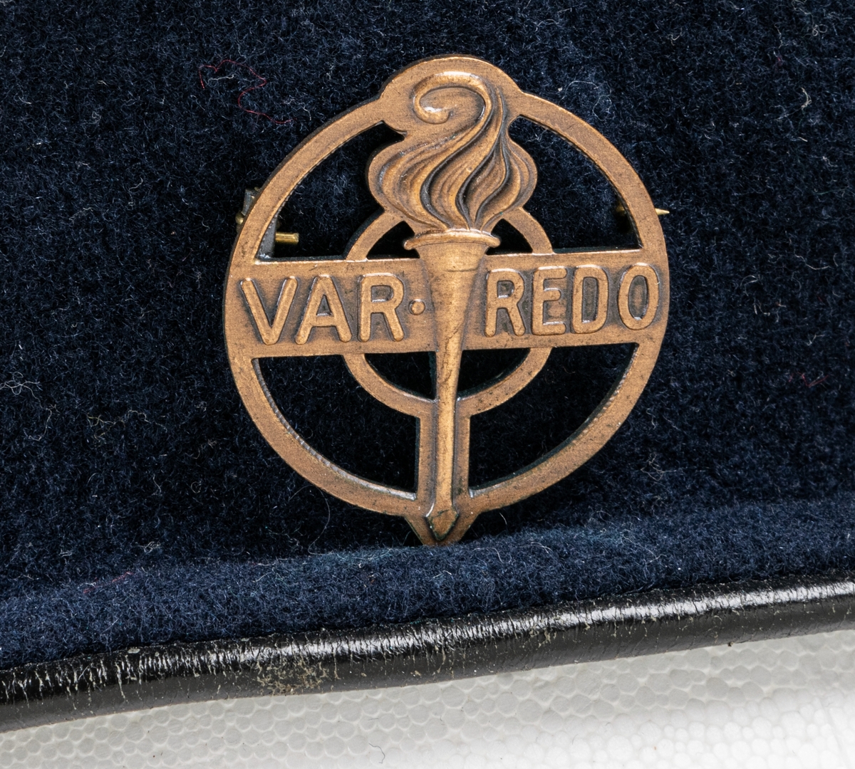 Blå filtbasker med läderkant. I sidan en metallpin "Var redo". Invändigt tryck: The Scout Shop, Trade Mark "Boy scouts" KANGOL, Cleaton Cumberland".
Storlek 7½/58.
Tejpbit med texten M. Ehrnberg, Bomhus.