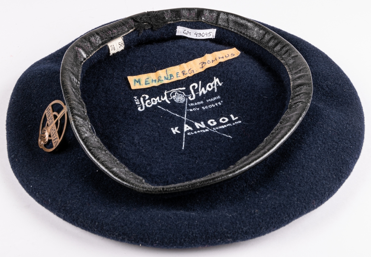 Blå filtbasker med läderkant. I sidan en metallpin "Var redo". Invändigt tryck: The Scout Shop, Trade Mark "Boy scouts" KANGOL, Cleaton Cumberland".
Storlek 7½/58.
Tejpbit med texten M. Ehrnberg, Bomhus.