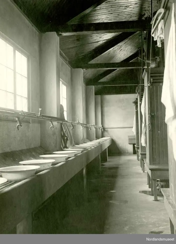 Sandnes. 
Fra badet i Grunnstollen, ca 1930. I tillegg til vaskefatene som var satt ut var det også dusjer der. Bildet viser at det var høyt opp under taket. Det til dels våte arbeidstøyet ble, etter arbeidsdagens slutt heist opp og hang under taket til neste arbeidsdag. Det var varmt på badet og når man kom på arbeid igjen neste gang så var det delvis våte tøyet som ved forrige skifts sluttet var hengt oppe under taket blitt tørt. 

De klærne man gikk til og fra arbeidet i oppbevarte hver mann i sitt låsbare skap. 

Foto Ukjent.