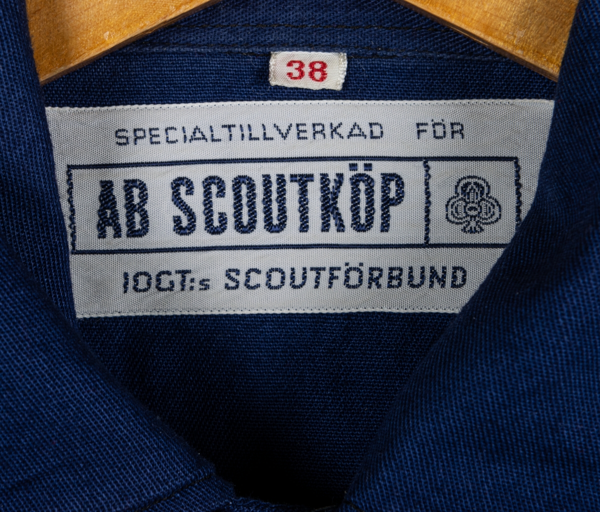 Blå scoutskjorta av bomull. Knäppning på bröstet samt fickor med IOGT-pin på den vänstra. Tygmärke på ena fickan. På höger axel tygmärke: "Bomhus", på vänster axel märke med brinnande fackla och texten "Var redo", och "Seniorscout". Runt nacken en röd sjal med vit kant samt en blåvit snodd med svart visselpipa.

I nacken vävd etikett: "Specialtillverkad för AB SCOUTKÖP, IOGT:s scoutförbund".
Storlek 38.