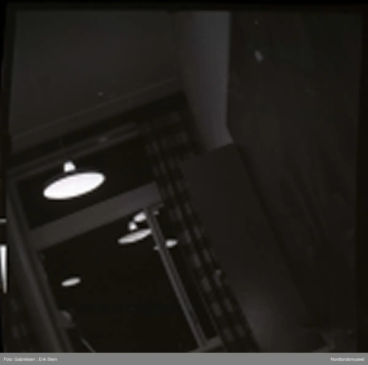 Fotografi av noen vinduer med gardiner i et klasserom 
i en skole og en tavle på veggen og noen lamper som henger
i taket som man ser i et speilbilde på vinduene i klasserommet