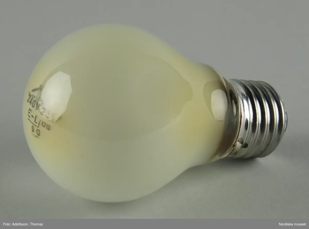 a) Bordslampa av svart pulverlackerat stål. Smal cylindrisk skärm vidgar sig nedåt till asymmetrisk trumpetform. Smal cylindrisk fot fäst i närmast oval fot med runt utsparat hål. Strömbrytare på foten, svart filt under densamma. Sladd av svart plast med stickpropp. Lampfattning E27 med b) isittande glödlampa. 

Mindre skrapmärken framtill på foten.
/Maria Maxén 2021-12-20