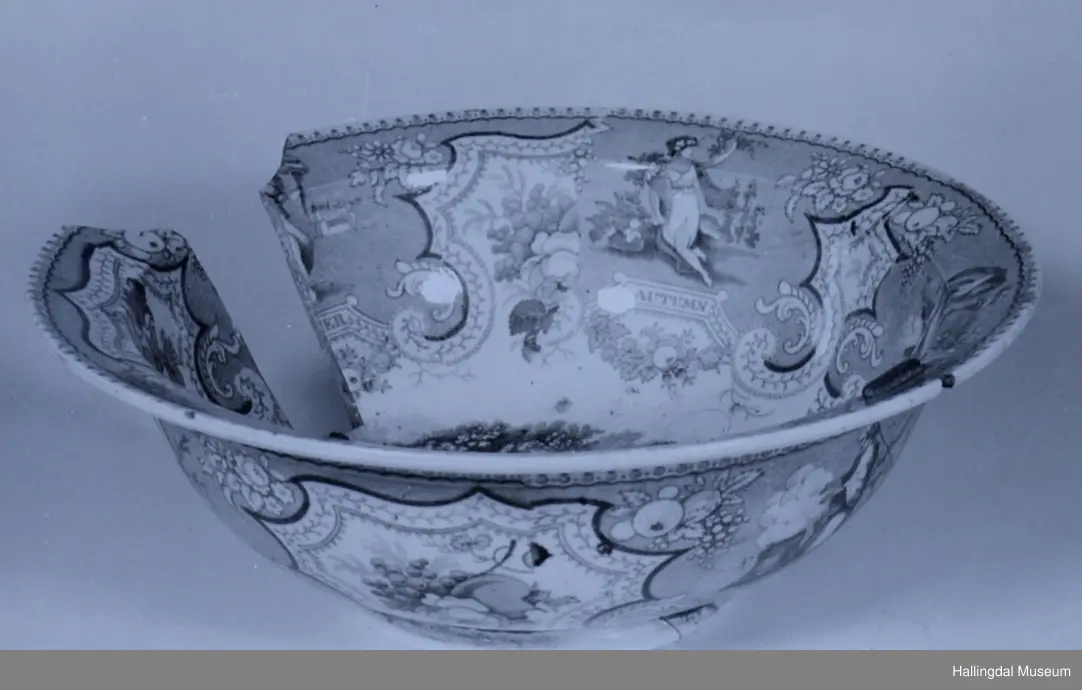 Flint? Hvitt, rundt, fotring. Utbuket side. markert kant med blå dekorasjoner. I bunnen landskap med jeger, symboliserende "april". Veggen innv. og utv. - blomsterklaser omgitt av knekkete bånd, mellom dem kvinnefigurer. Sprukket og klinket. Et stykke mangler. Bunnen stemplet: "Patterson" 12.

R.B.S.