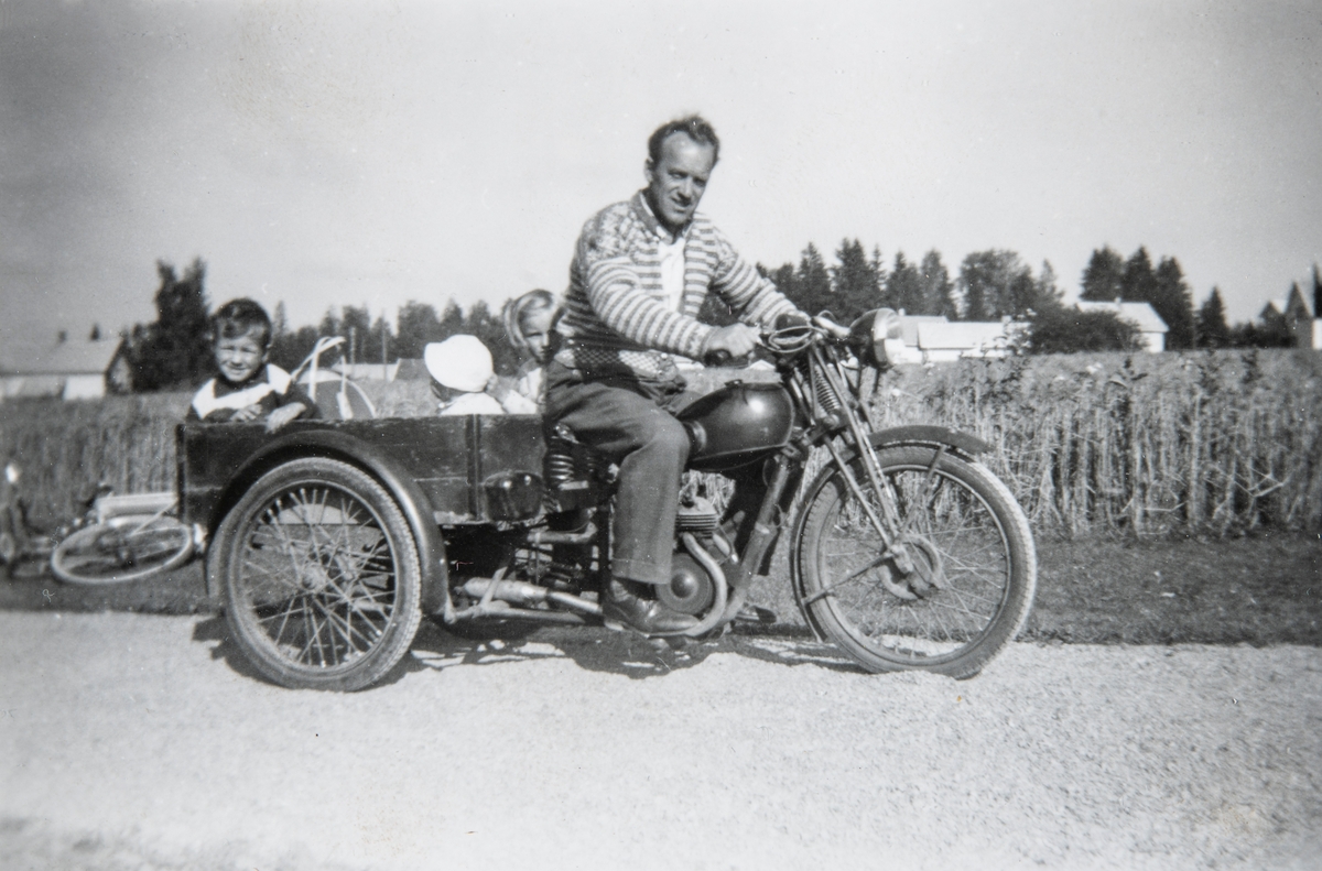 Arne Furulund (1919-2002) på en 3 hjuls motorsykkel med lasteplan. Barna Wenche Furulund, Edgar Furulund og Trond Furulund i "kassa". Bildet er tatt i 1959.
