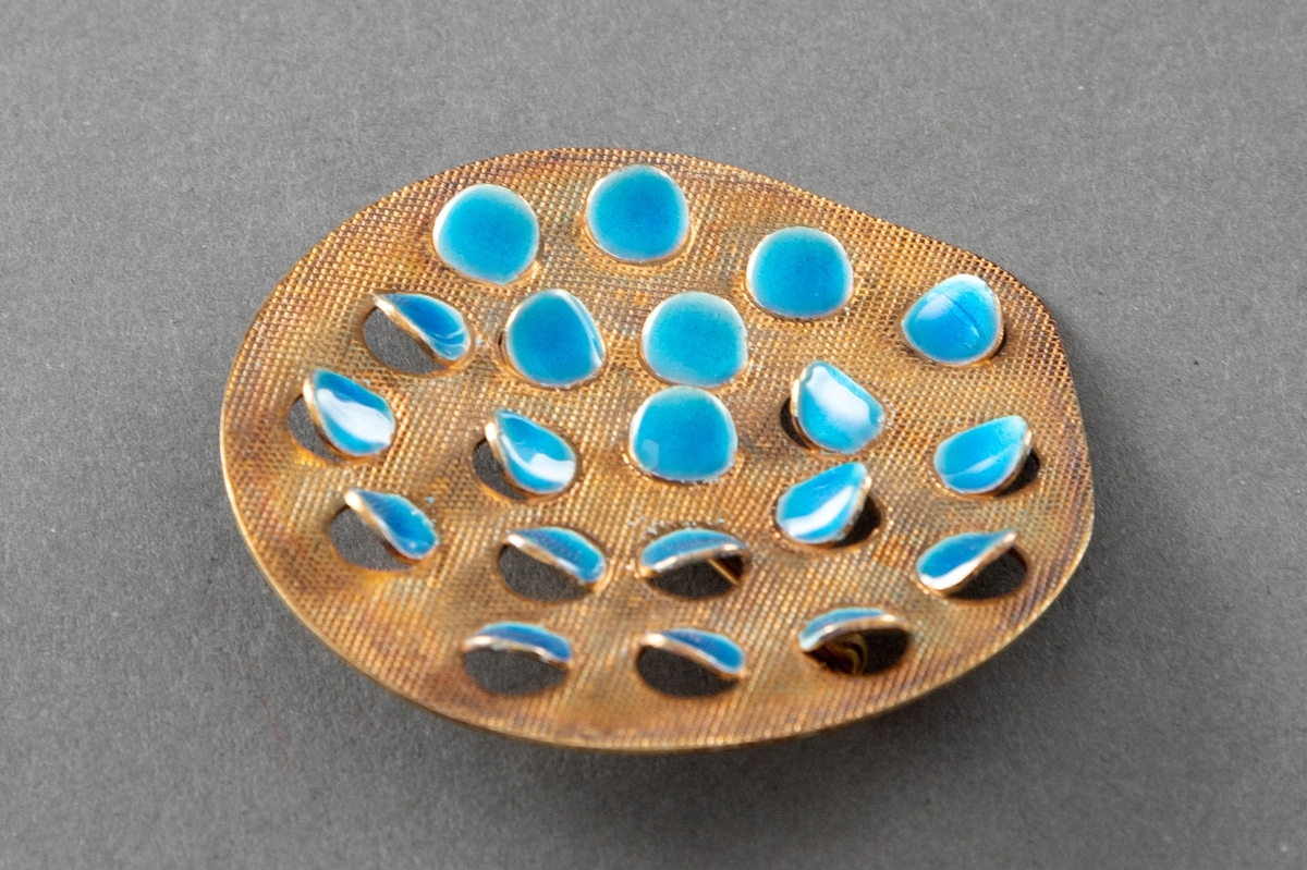 Brosje bestående av en tilnærmet rund plate i forgylt sølv med rutemønstret overflate og halvgjennombrutte, runde flak dekket med turkis emalje som åpner seg utover.