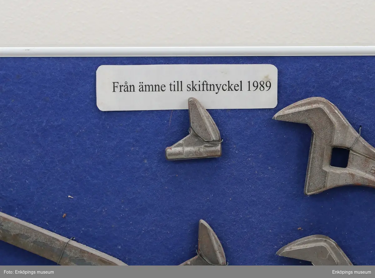 "Från ämne till skiftnyckel 1989". Tavla med metallram, blå textil.