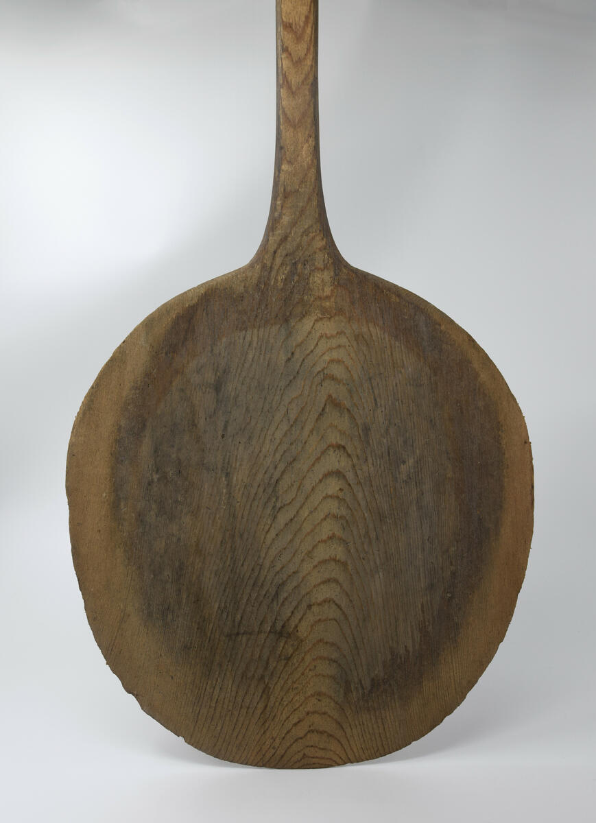 Brödspade, av björkträ gjord i ett enda stycke. Oval skiva med långt skaft. Skivans storlek 0,36 x 0,40 m. Nött länst hela skaftet och i toppen av skivan.