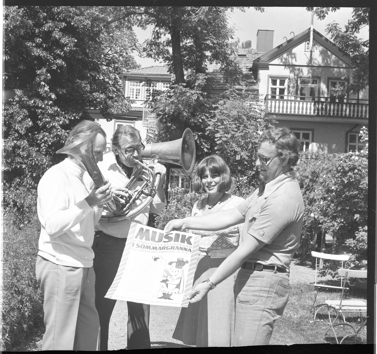 Två män med blåsinstrument, en kvinna och ytterligare en man som håller upp en affisch: "Musik i Sommargränna".