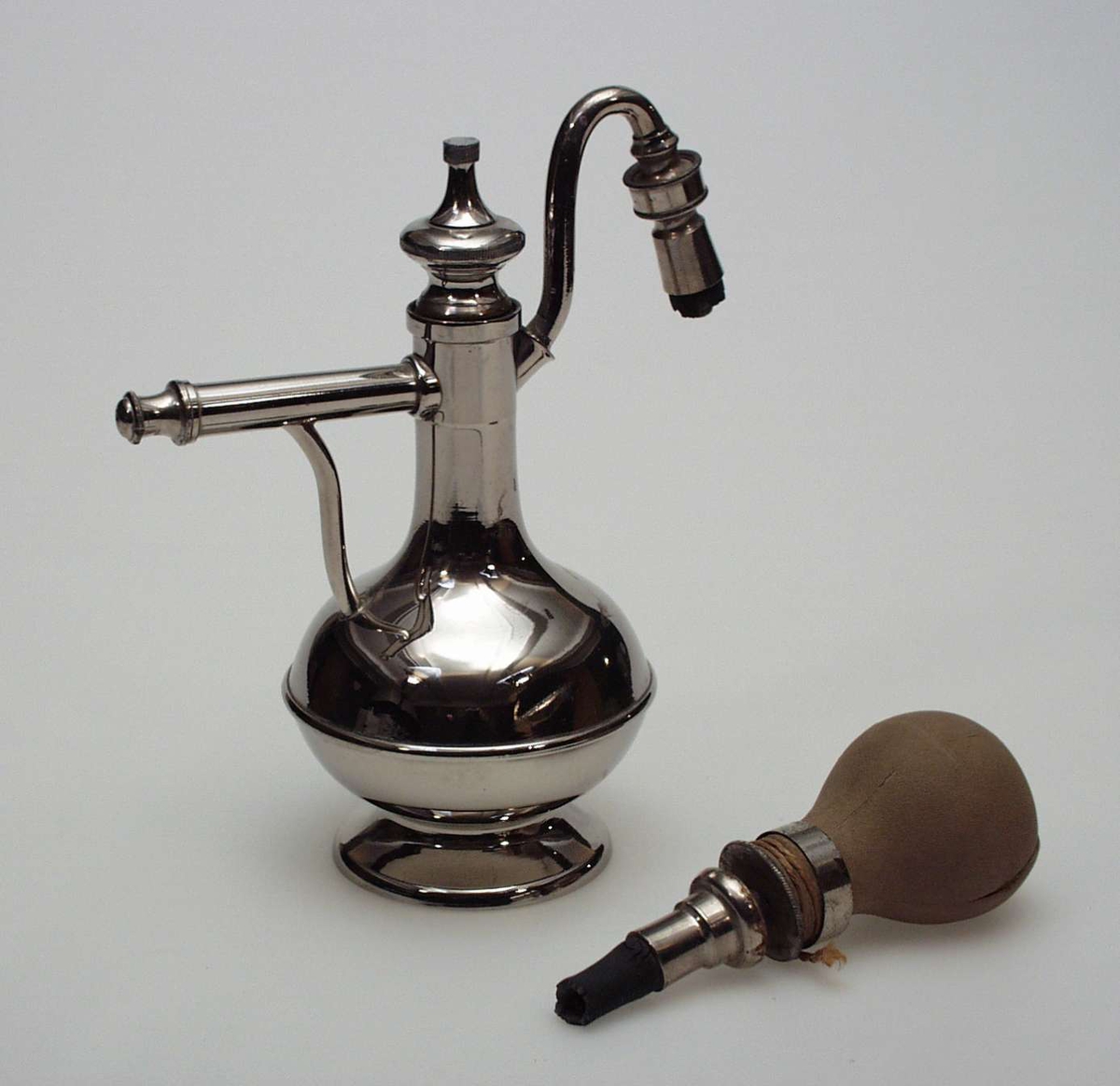 Sprøyte laget i nikkel med gummiballong. Gjenstanden har kannefasong.