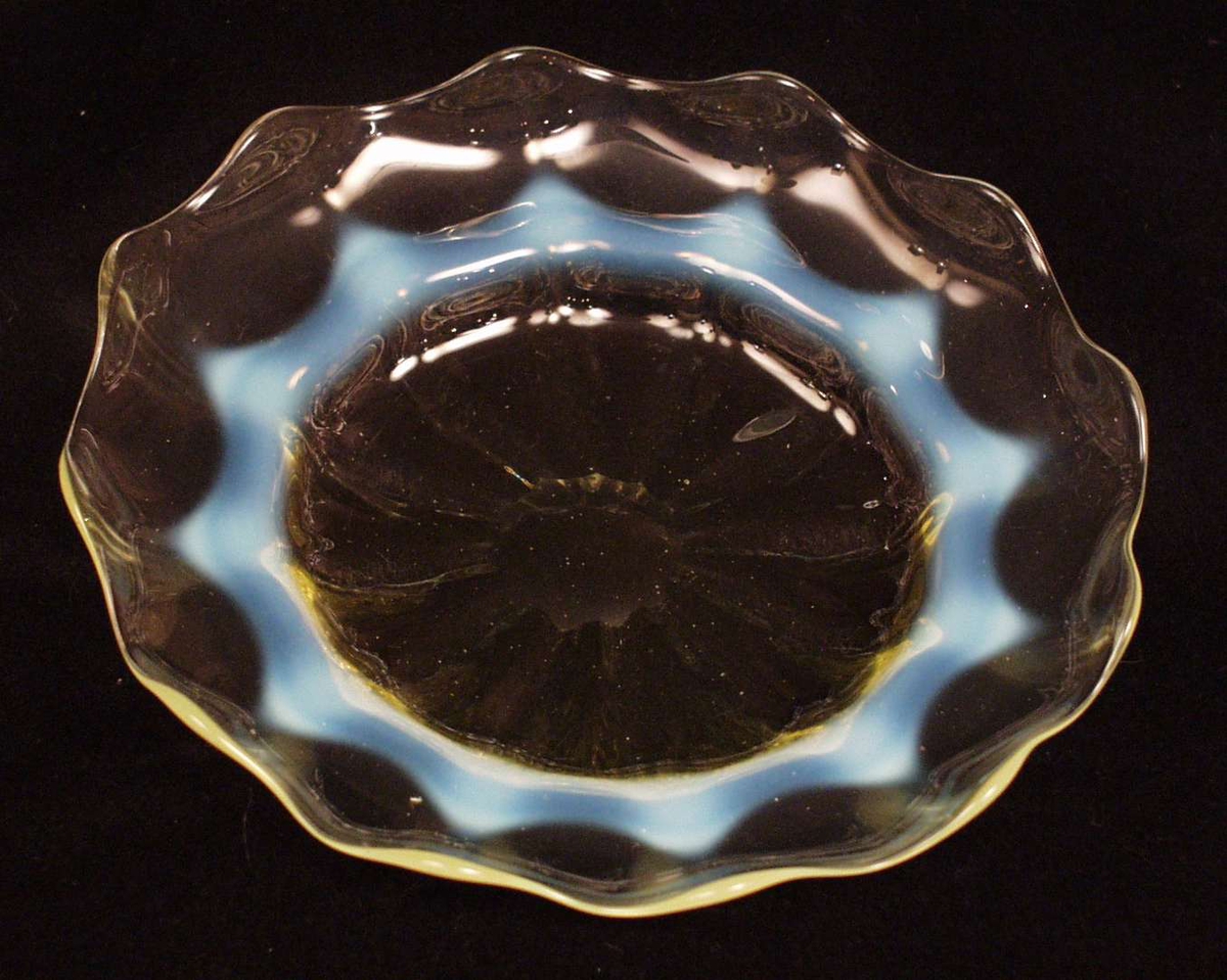 Skålen er laget av gult glass, med tunget kant. 