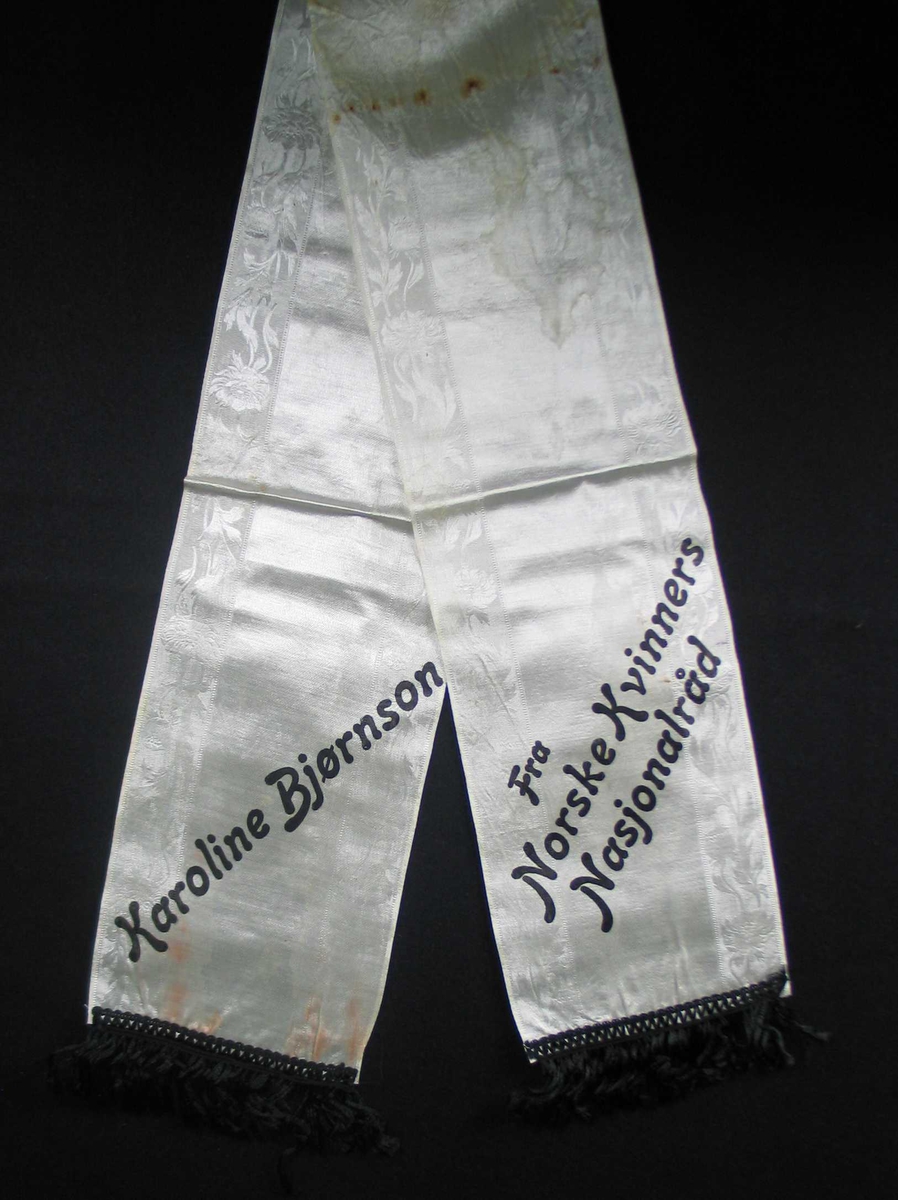 Begravelsessløyfe hvit mønstret silke med svart tekst.