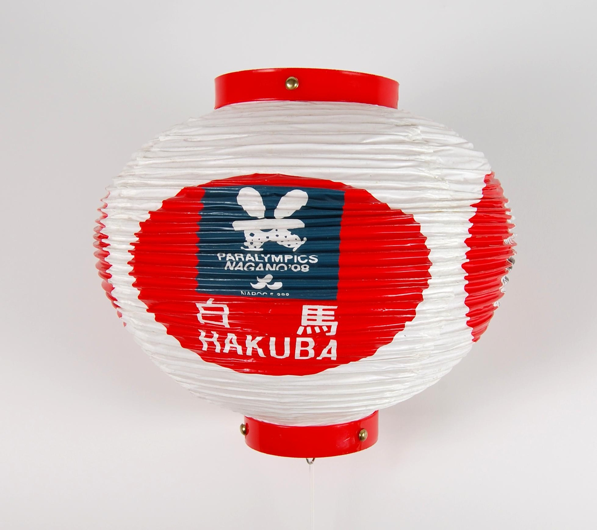 Rund lykt med logo for Paralympics i Nagano i 1998 og de olympiske vinterleker i Nagano i 1998. Lykta kan foldes sammen. Lykta er noe slitt. Den har blant annet noen hull.