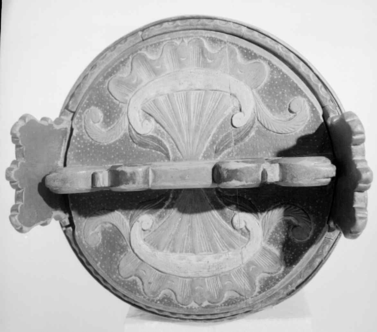 Grønnmalt ambar med to flate grønne gjorder. Mellom dem et felt med skåret og rødmalt akantusbord. Skåret og malt akantusmotiv på føttene - sju intakte og en defekt. Akantus skurd på ørene og skåret lokk med håndtak. Mangler stengsel for lokket. Påmalt innskrift som er slitt og uleselig på et av båndene. Skåret perlerad langs ene kanten.