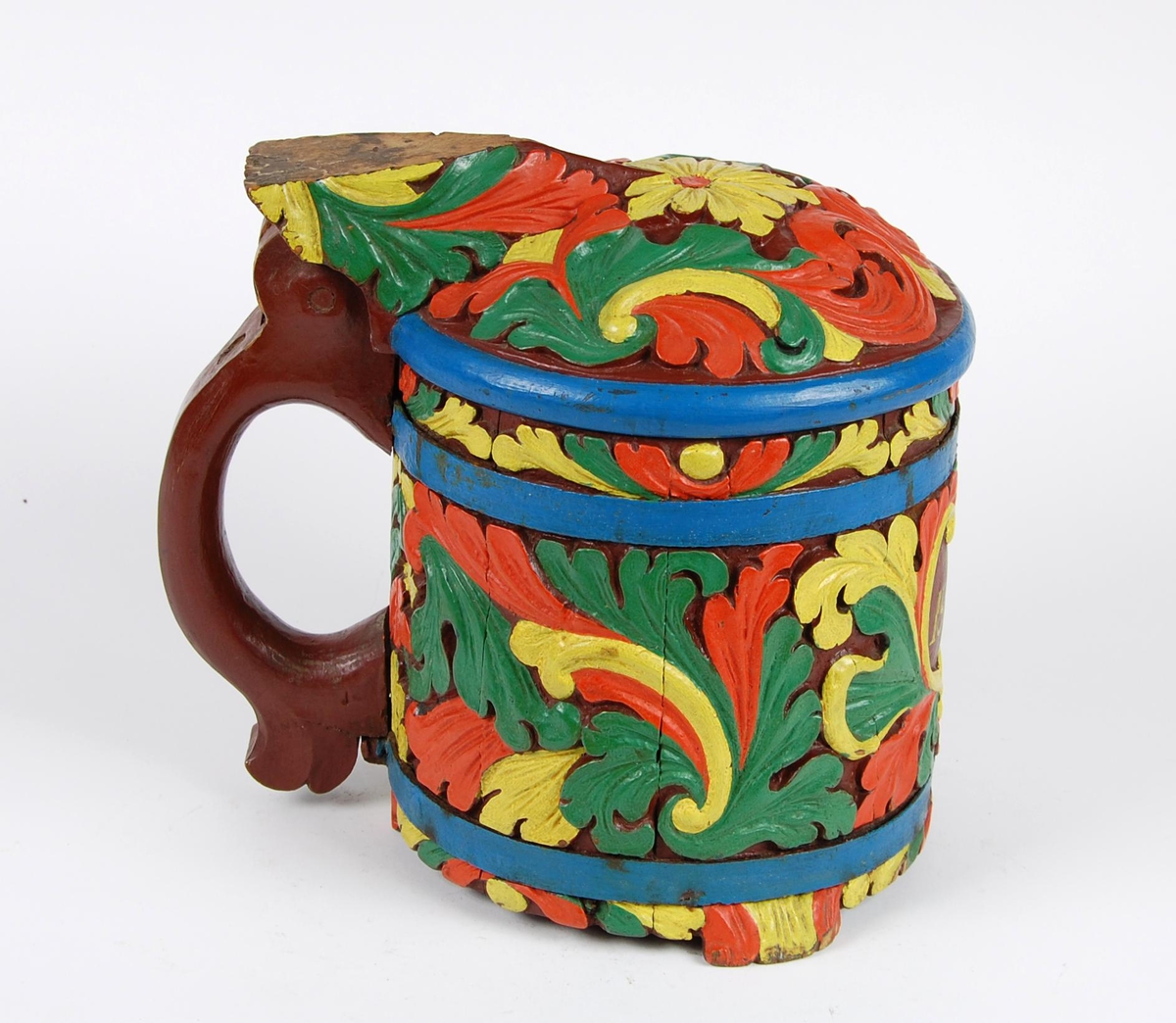 Kanne av staver. Lokk med gule, grønne og røde blader, blåmalt kant. Korpus med en blåmalt metallgjord oppe og nede, gule, grønne og røde akantusblader, brunmalt hjerteformet felt med innskriften 1865. Brunmalt hank. Tre røde og gule føtter.